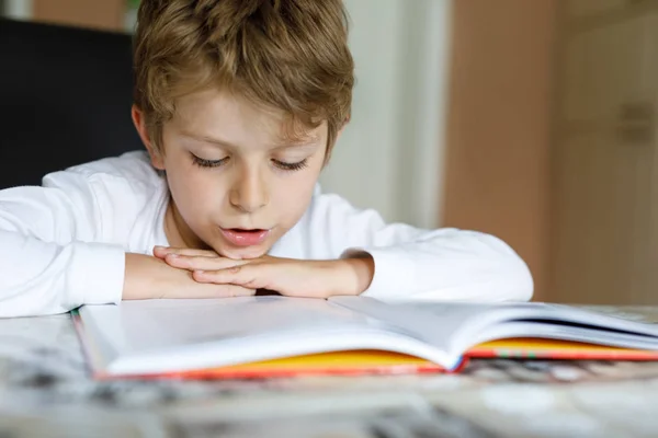 Little blonde school kid boy reading a book at home. Child interested in reading magazine for kids. Leisure for kids, building skills and education concept — Stock Photo, Image