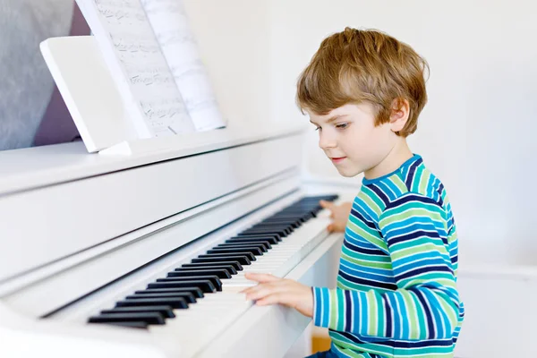 Beautiful little kid boy with headphones playing piano in living room or music school. Preschool child having fun with learning to play music instrument. Education, skills concept — Stock Photo, Image