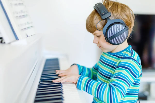 Красивый маленький мальчик в наушниках играет на пианино в гостиной или музыкальной школе. Детям дошкольного возраста весело учиться играть на музыкальном инструменте. Образование, концепция навыков — стоковое фото