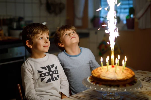 Duas crianças lindas, meninos pré-escolares comemorando aniversário e soprando velas em bolo cozido em casa, em casa. Festa de aniversário para irmãos crianças. Gêmeos felizes sobre presentes. — Fotografia de Stock