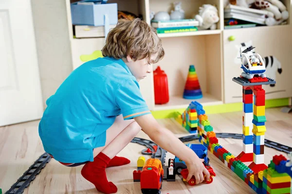 Menino loiro adorável brincando com blocos de plástico coloridos e criando estação de trem. Criança se divertindo com a construção de brinquedos ferroviários em casa .. — Fotografia de Stock