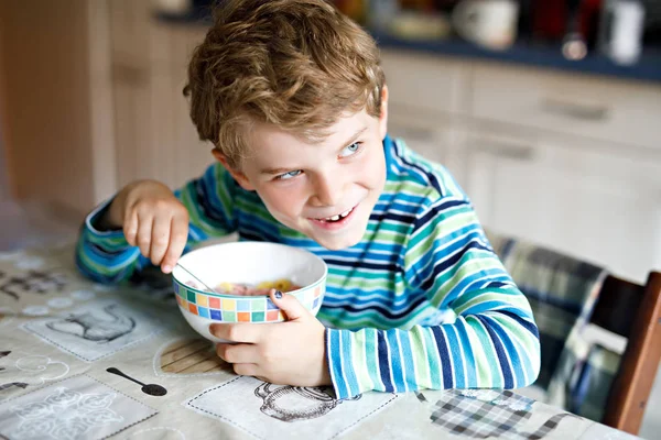Menino da escola louro adorável comendo cereais com leite e bagas no café da manhã ou almoço. Alimentação saudável para crianças, alunos. Na cantina da escola ou em casa — Fotografia de Stock
