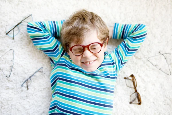 Close-up portrait of little blond kid boy with different eyeglasses on white background. Happy smiling child in casual clothes. Childhood, vision, eyewear, optician store. Boy choosing new glasses. — Stock Photo, Image