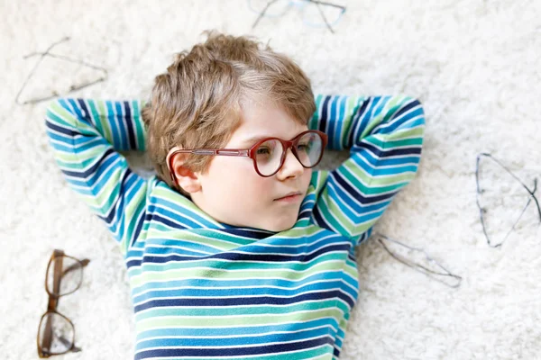 Close-up portrait of little blond kid boy with different eyeglasses on white background. Happy smiling child in casual clothes. Childhood, vision, eyewear, optician store. Boy choosing new glasses. — Stock Photo, Image