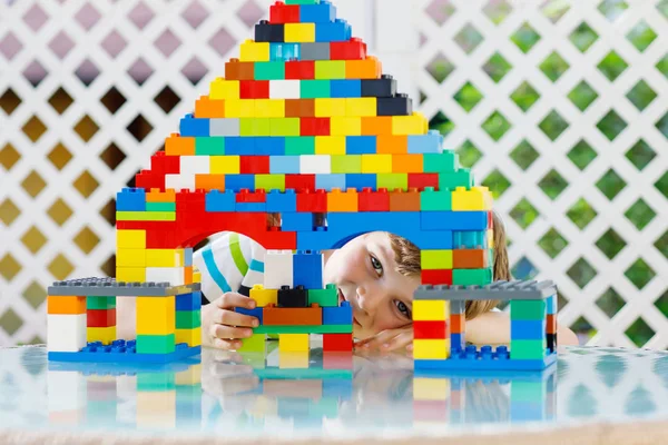 Criança loira brincando com muitos blocos de plástico coloridos. Menino pré-escolar adorável vestindo camisa colorida e se divertindo com a construção de um grande castelo e criando uma casa — Fotografia de Stock