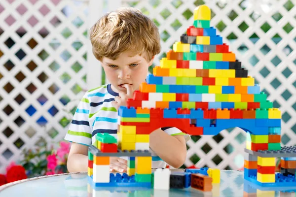 Criança loira brincando com muitos blocos de plástico coloridos. Menino pré-escolar adorável vestindo camisa colorida e se divertindo com a construção de um grande castelo e criando uma casa — Fotografia de Stock