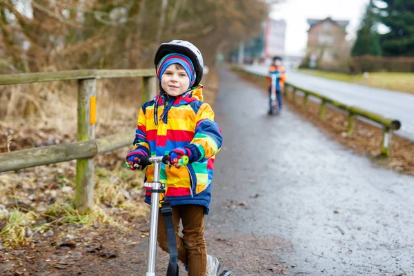 Cute little preschool kid boy riding on scooter in park nature. children activities outdoor in winter, spring or autumn. funny happy child in colorful fashion clothes and with helmets. High speed. — Stock Photo, Image