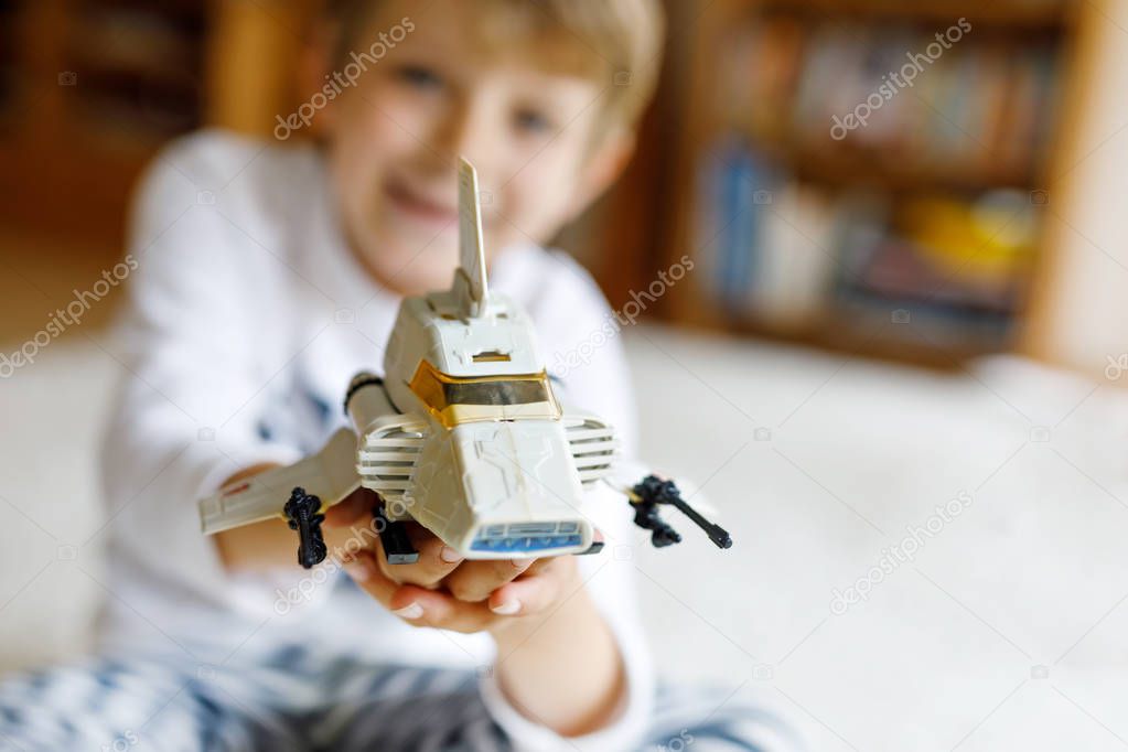 Happy little kid boy playing with space shuttle toy. Cute child in having fun in the morning before school. Selective focus on old plastic toy. Blond kid on background.
