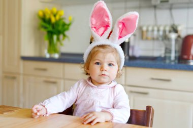 Paskalya tavşanı kulakları takan tatlı küçük kız renkli pastel yumurtalarla oynuyor. Mutlu bebek hediyeleri açıyor. Pembe elbiseli sevimli, sağlıklı çocuk aile tatilinin tadını çıkarıyor.