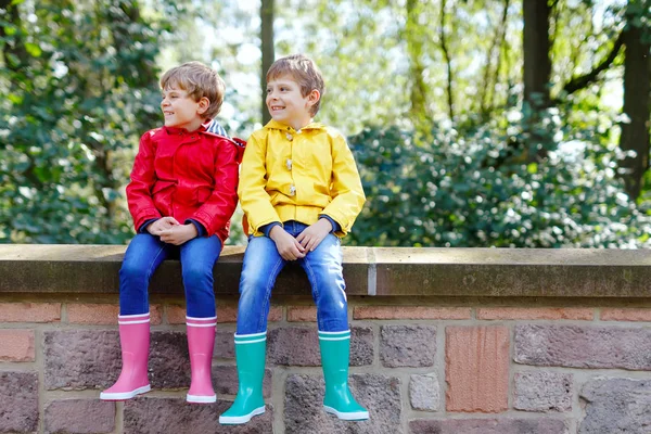 Two little kids boys, cute siblings in colorful rain boots. Close-up of children in different rubber boots and jackets. Footwear for rainy fall. Healthy twins and best friends having fun outdoors — Stock Photo, Image