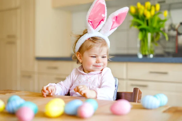 Cute little toddler girl wearing Easter bunny ears playing with colored pastel eggs. Happy baby child unpacking gifts. Adorable healthy smiling kid in pink clothes enjoying family holiday — Stock Photo, Image