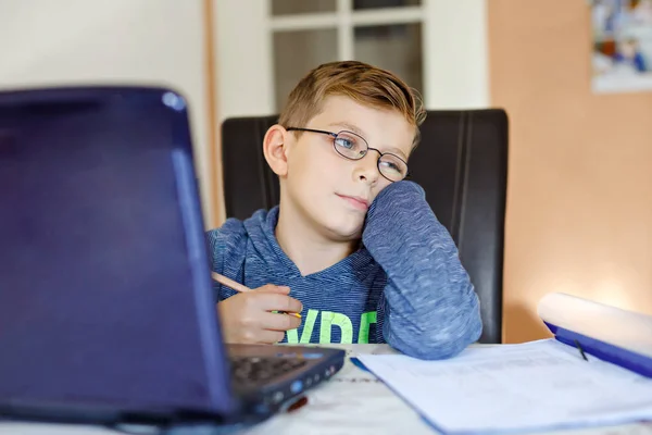 Trött ledsen kid boy med glasögon att göra skolan läxor hemma med notebook. Deprimerade barn skriva uppsats med hjälp av internet. Overhelmed skolbarn koncept. — Stockfoto
