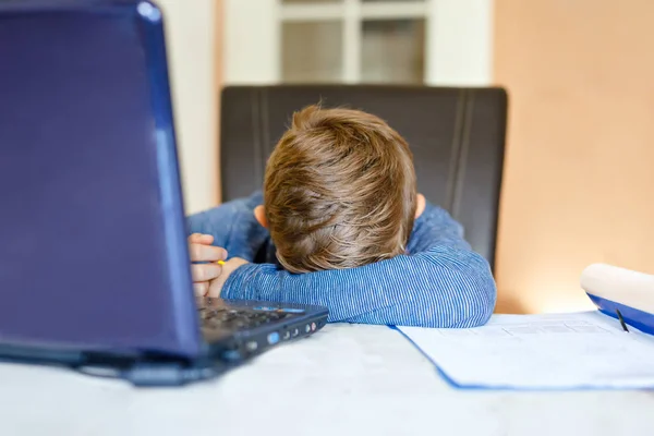 Tired sad kid boy with glasses making school homework at home with notebook. Depressed child writing essay with helping of internet. Overhelmed schoolchildren concept. — Stock Photo, Image