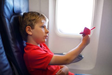 Küçük çocuk çocuk uçakta uçuş sırasında kırmızı kağıt uçak ile oynuyor. Uçak tarafından bir pencere içinde oturan çocuk. Aile tatile gidiyor