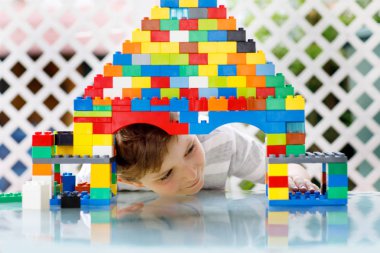 Renkli plastik bloklarla oynayan küçük sarışın çocuk. Sevimli kreş çocuğu renkli tişörtler giyiyor ve büyük bir kale inşa edip bir ev yaratarak eğleniyor.