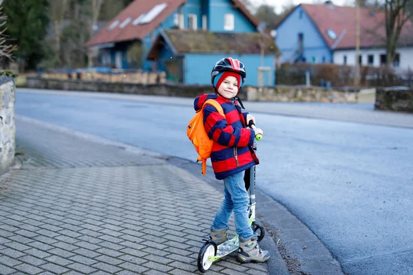 Leuke kleuter die op een scooter naar school rijdt. activiteiten voor kinderen in de buitenlucht in de winter, lente of herfst. grappig vrolijk kind in kleurrijke mode kleding en met helm. Hoge snelheid. — Stockfoto