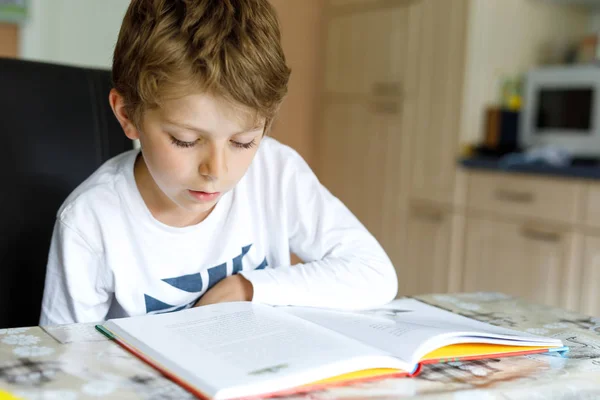 En blond skolpojke som läser en bok hemma. Barn intresserade av att läsa tidningen för barn. Fritid för barn, bygga färdigheter och utbildning koncept.. — Stockfoto