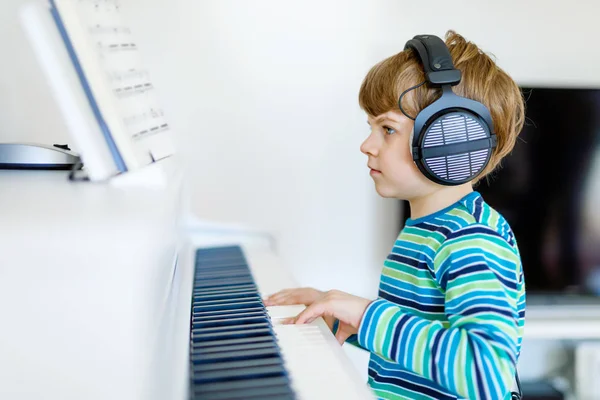 Güzel bir çocuk çocuk oturma odası veya müzik okulu piyano kulaklıklarla. Okul öncesi çocuk müzik enstrüman çalmak öğrenme ile eğleniyor. Eğitim, beceri kavramı — Stok fotoğraf