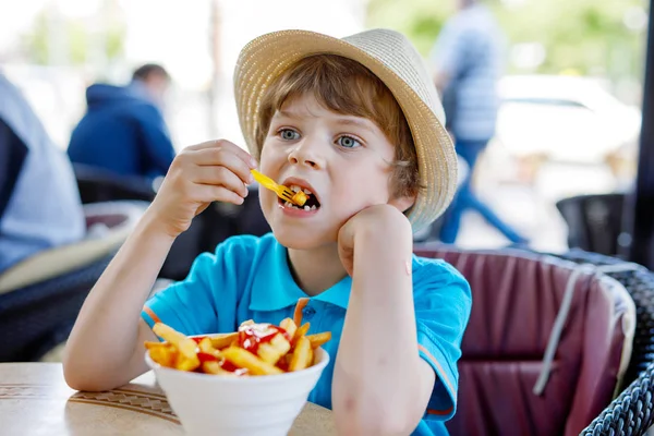 Chłopiec cute zdrowego dziecka przedszkola zjada ziemniaki frytki z keczupem, siedząc w kawiarni na świeżym powietrzu. Szczęśliwe dziecko Niezdrowe jedzenie w restauracji — Zdjęcie stockowe