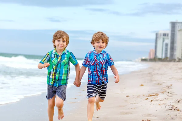 Dwóch szczęśliwych chłopców biegających po plaży oceanu. Śmieszne słodkie dzieci, rodzeństwo i najlepszych przyjaciół dokonywania wakacji i ciesząc się latem w burzliwy wietrzny dzień. Zdrowe dzieci na plaży w Miami, USA — Zdjęcie stockowe