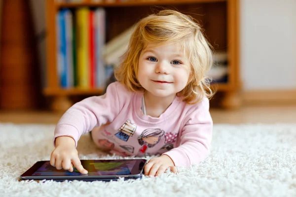 Menina bonito pequena criança brincando com tablet pc em casa. Almofada de bebê saudável tocando com os dedos, olhando desenhos animados e se divertindo com jogos educativos no computador. Conceito de desenvolvimento inicial — Fotografia de Stock