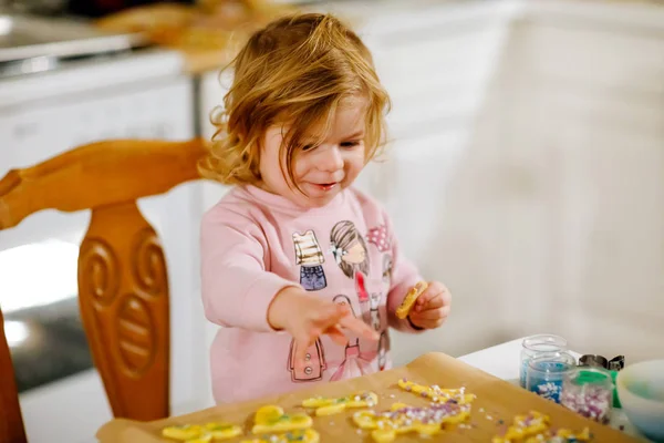 Cute little baby girl baking gingerbread Christmas cookies at home. Adorable blond child having fun in domestic kitchen. Traditional leisure with kids on Xmas. Toddler tasting dough. — Stock Photo, Image