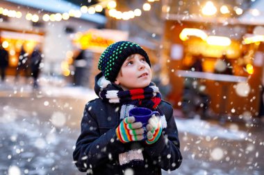 Küçük şirin çocuk Alman Noel pazarında sıcak çocuk kokteyli ya da çikolata içiyor. Almanya 'nın geleneksel aile pazarında mutlu bir çocuk renkli kışlık giysiler içinde gülen bir çocuk.