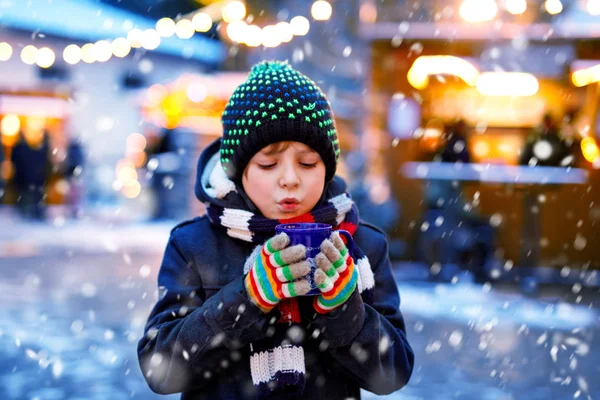 Niño lindo bebiendo ponche de niños calientes o chocolate en el mercado de Navidad alemán. Niño feliz en el mercado familiar tradicional en Alemania, niño risueño en ropa de invierno colorida —  Fotos de Stock