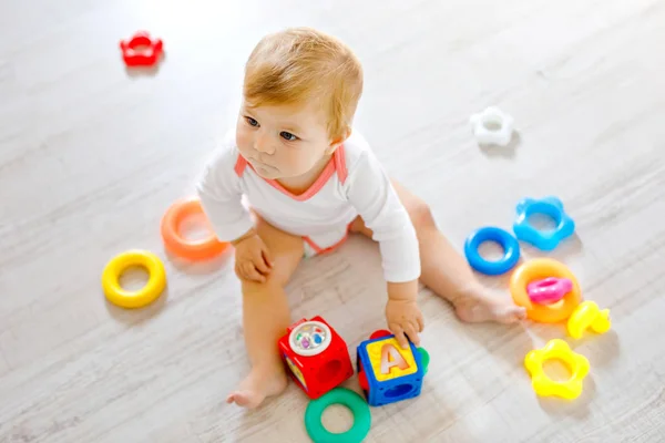 Adorável menina brincando com brinquedos educativos no berçário. Criança saudável feliz se divertindo com brinquedos diferentes coloridos em casa. Criança tentando construir pirâmide de plástico e usando blocos com letras — Fotografia de Stock