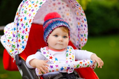 Mavi, sıcacık şapkalı, bebek arabasında ya da bebek arabasında oturan ve annesini bekleyen küçük, sağlıklı bir kız bebek. Mavi gözlü mutlu çocuk. Küçük kızım ailesiyle yürüyüşe çıkıyor.