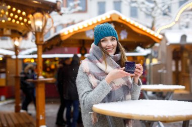Güzel genç kadın sıcak panç içiyoruz mulled şarap Alman Noeli piyasada. Kış giysileri arka planda kış kar günü Münih, Almanya ışıkları ile mutlu kızı.