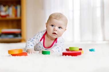 Yeni doğmuş şirin bebek beyaz arka planda renkli tahta çıngıraklı oyuncak topuyla oynuyor. Yeni doğmuş bir çocuk, kameraya bakan küçük bir kız. Aile, yeni hayat, çocukluk, başlangıç konsepti.