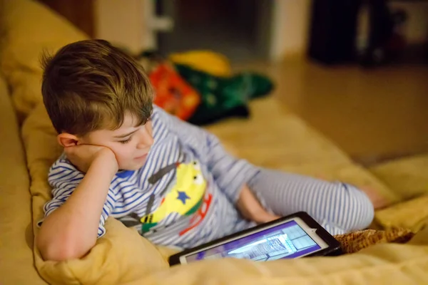 Niño de la escuela haciendo tarea con la tableta. Lectura y aprendizaje escolar con ordenador, búsqueda de información en Internet y búsqueda de dibujos animados antes de dormir e ir a la cama —  Fotos de Stock