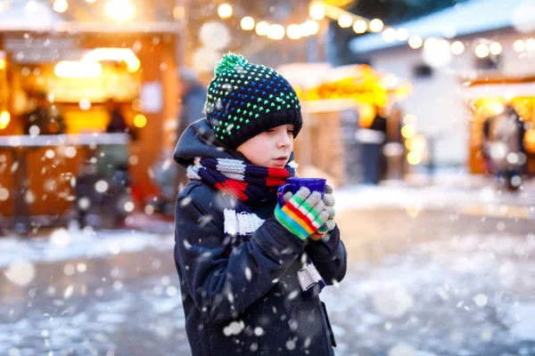 Little cute kid boy drinking hot children punch or chocolate on German Christmas market. Happy child on traditional family market in Germany, Laughing boy in colorful winter clothes — Stock Photo, Image