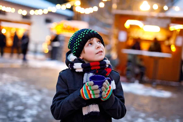 Petit garçon mignon qui boit du punch ou du chocolat chaud pour enfants sur le marché de Noël allemand. Enfant heureux sur le marché familial traditionnel en Allemagne, Rire garçon en vêtements d'hiver colorés — Photo