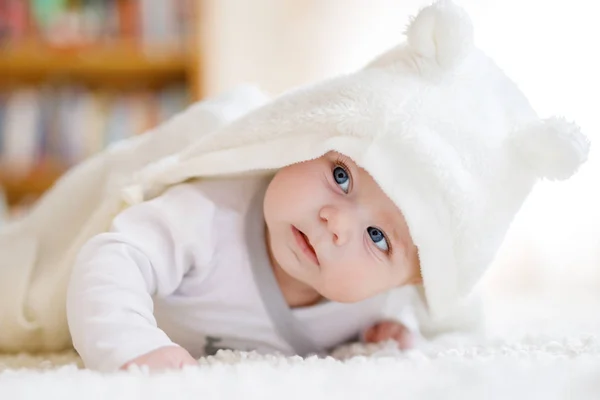 Babymeisje met blauwe ogen dragen witte handdoek of winter overal in witte zonnige slaapkamer. Pasgeboren kind ontspannen in bed. Crèche voor kinderen. Textiel en beddengoed voor kinderen. Nieuwe geboren jongen met speelgoed Beer — Stockfoto