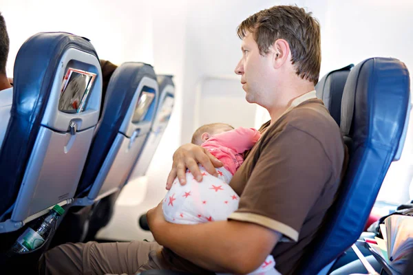 Joven padre cansado y su hija llorando durante el vuelo en avión de vacaciones. Papá sosteniendo a la niña del brazo. Viajes aéreos con concepto de bebé, niño y familia — Foto de Stock