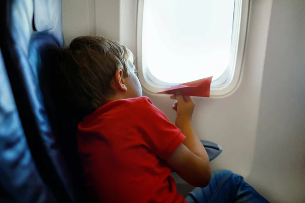 Niño jugando con avión de papel rojo durante el vuelo en avión — Foto de Stock