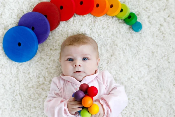 Cute adorable newborn baby playing with colorful wooden rattle toy ball on white background. New born child, little girl looking ath the camera. Family, new life, childhood, beginning concept. — Stock Photo, Image