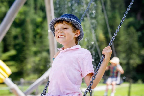 Lustiger Junge, der Spaß mit Kettenschaukel auf dem Spielplatz hat, während er nass mit Wasser bespritzt wird. Kind schaukelt an Sommertagen. Aktive Freizeit mit Kindern. Glücklich weinender Junge mit Regentropfen im Gesicht. — Stockfoto