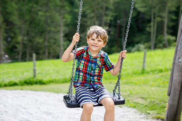 Rolig pojke som har kul med kedja swing på utomhus lekplats samtidigt som våt stänkt med vatten. barn som svingar på sommardagen. Aktiv fritid med barn. Glad gråtande pojke med regn droppar i ansiktet. — Stockfoto