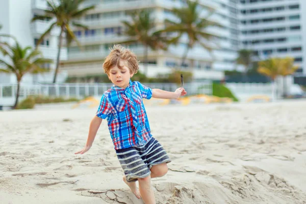 Portrait of happy little kid boy on the beach of ocean. Funny cute child making vacations and enjoying summer. Healthy boy on the beach of Miami USA on stormy windy day. — Stock Photo, Image