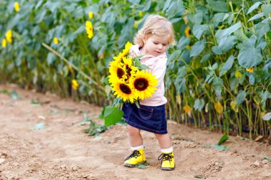 Sarı çiçekli ayçiçeği alan sevimli sevimli bebek kız. Güzel bebek çocuk sarı tüyleri ile. Gülümseyen ve buket tutan mutlu sağlıklı küçük kızı. Yaz sonu üzerinde açık portre