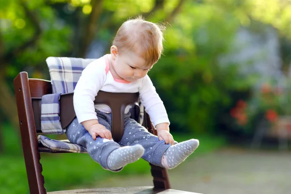 Söt bedårande baby flicka sitter i barnstol utomhus. Beatuiful barn 6 månader i hem trädgård, spelar på varm solig dag. Friskt barn ler och skrattar. — Stockfoto