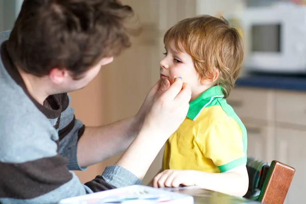 Giovane papà pittura bandiera sul viso del piccolo figlio per il calcio o gioco di calcio. — Foto Stock