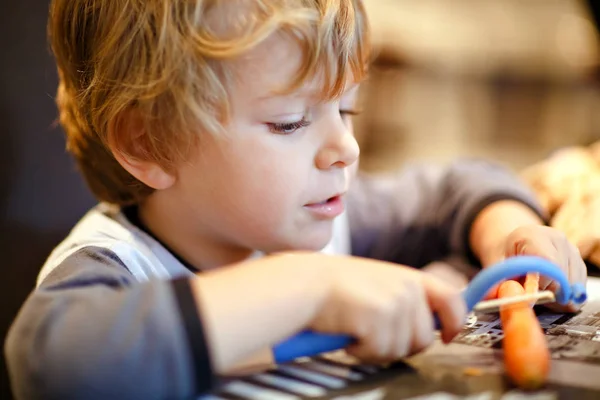 Lindo niño pela zanahorias frescas. Adorable niño sano comiendo bocadillo de verduras. Niño feliz degustación de alimentos saludables . —  Fotos de Stock