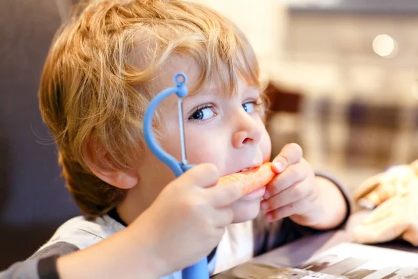 Ładny mały chłopiec dziecko złuszcza świeże marchewki. Urocze dziecko zdrowe jedzenie warzyw. Szczęśliwe dziecko degustację zdrowej żywności. — Zdjęcie stockowe