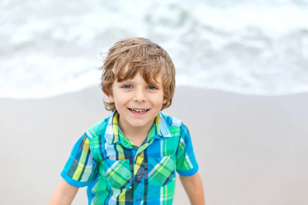 Portrait of happy little kid boy on the beach of ocean. Funny cute child making vacations and enjoying summer. Healthy boy on the beach of Miami USA on stormy windy day. — Stock Photo, Image