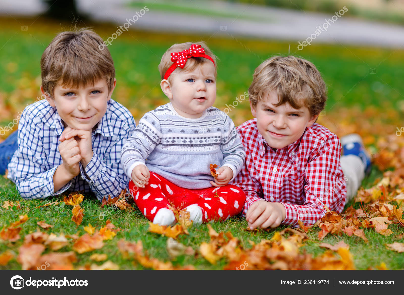 To små glade unggutter med nyfødt lillesøster. Søsken på gress i høstparken  med gult og rødt lønneblad. Barn som knytter bånd. Familie med tre barn . –  stockfoto © romrodinka #236419774, image size:1600x1167
