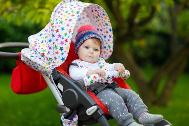 Mavi, sıcacık şapkalı, bebek arabasında ya da bebek arabasında oturan ve annesini bekleyen küçük, sağlıklı bir kız bebek. Mavi gözlü mutlu çocuk. Küçük kızım ailesiyle yürüyüşe çıkıyor..
